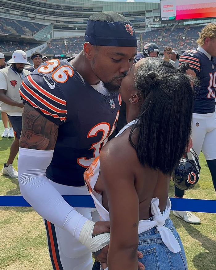 Chicago Bears player in uniform kissing a woman on the field after a game, with teammates in the background. Chicago Bears player in uniform kissing a woman on the field after a game, with teammates in the background.