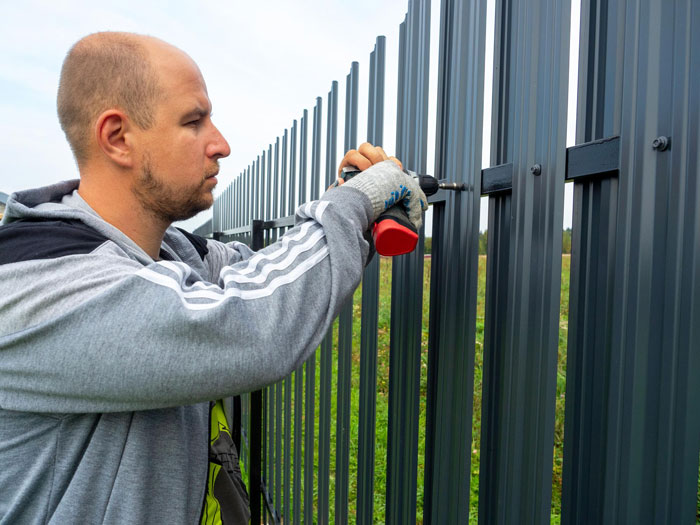 Man wearing gloves using a drill to install a metal fence outdoors, illustrating Karen Petty fence revenge concept. Man wearing gloves using a drill to install a metal fence outdoors, illustrating Karen Petty fence revenge concept.