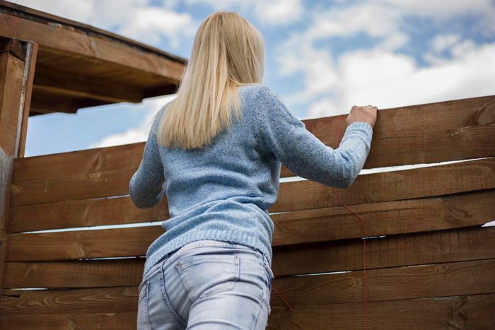 Woman in a blue sweater leaning over a wooden fence, representing Karen petty fence revenge concept outdoors. Woman in a blue sweater leaning over a wooden fence, representing Karen petty fence revenge concept outdoors.