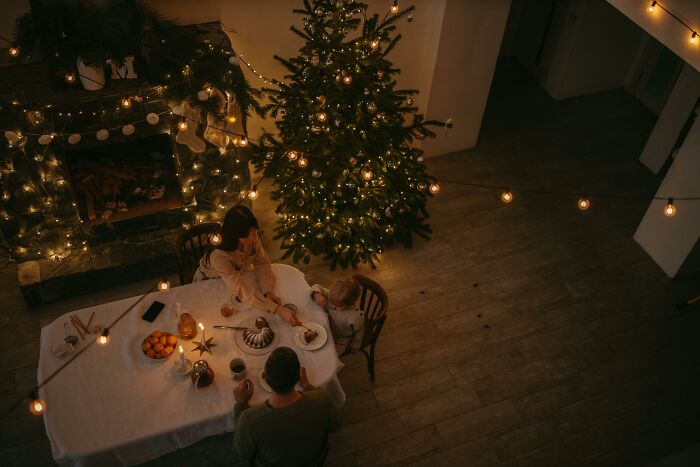 Family enjoying a cozy Christmas dinner beside a decorated tree with festive string lights and holiday treats. Family enjoying a cozy Christmas dinner beside a decorated tree with festive string lights and holiday treats.