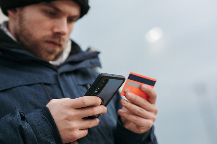 Man using phone and credit card outdoors, illustrating a glitch in the system being exploited digitally.