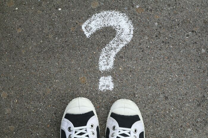 White sneakers standing on asphalt next to a large chalk question mark, symbolizing pub trivia night questions.