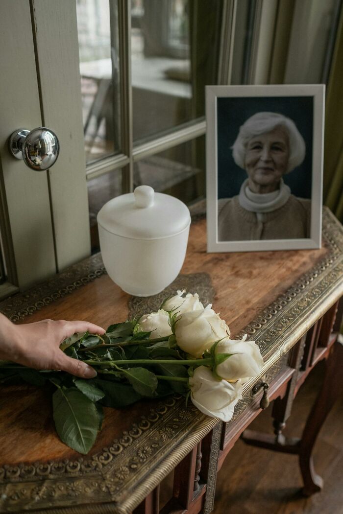 White urn and framed photo on wooden table with hand holding white roses, representing unusual personal belongings in lost and found.