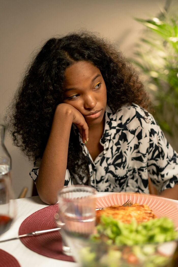 Teen girl with curly hair looking frustrated at the dinner table, illustrating modern parenting trends challenges.