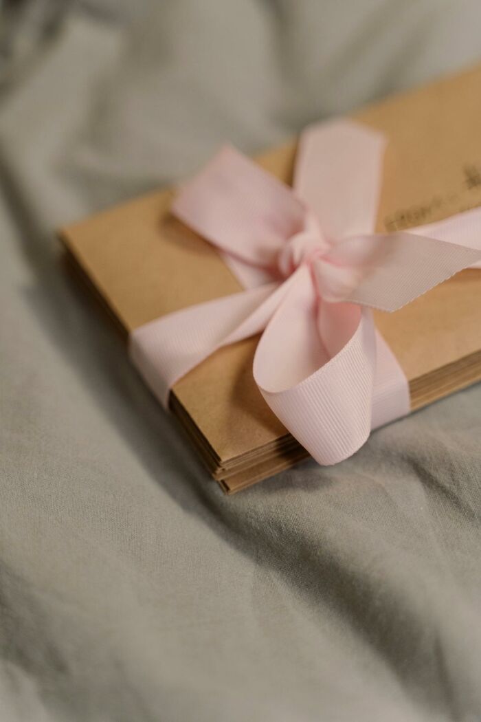 Stack of lost brown envelopes tied with a pink ribbon placed on a soft gray fabric surface, people never came back for them.