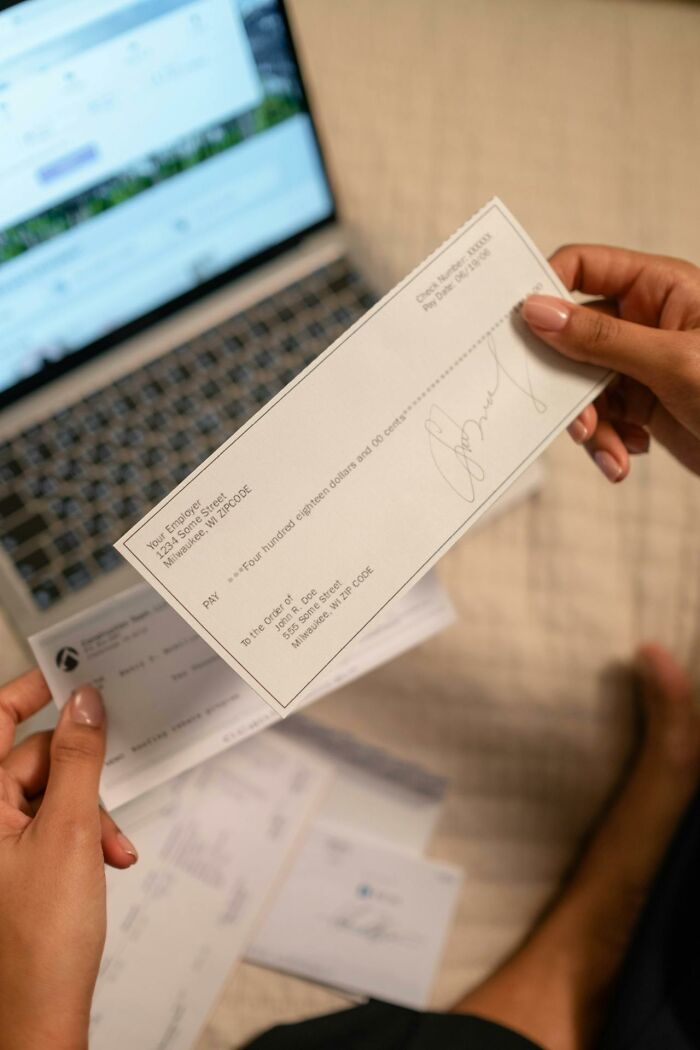 Person holding a signed check near a laptop while reviewing bills, illustrating entitlement over gummy candies issue.