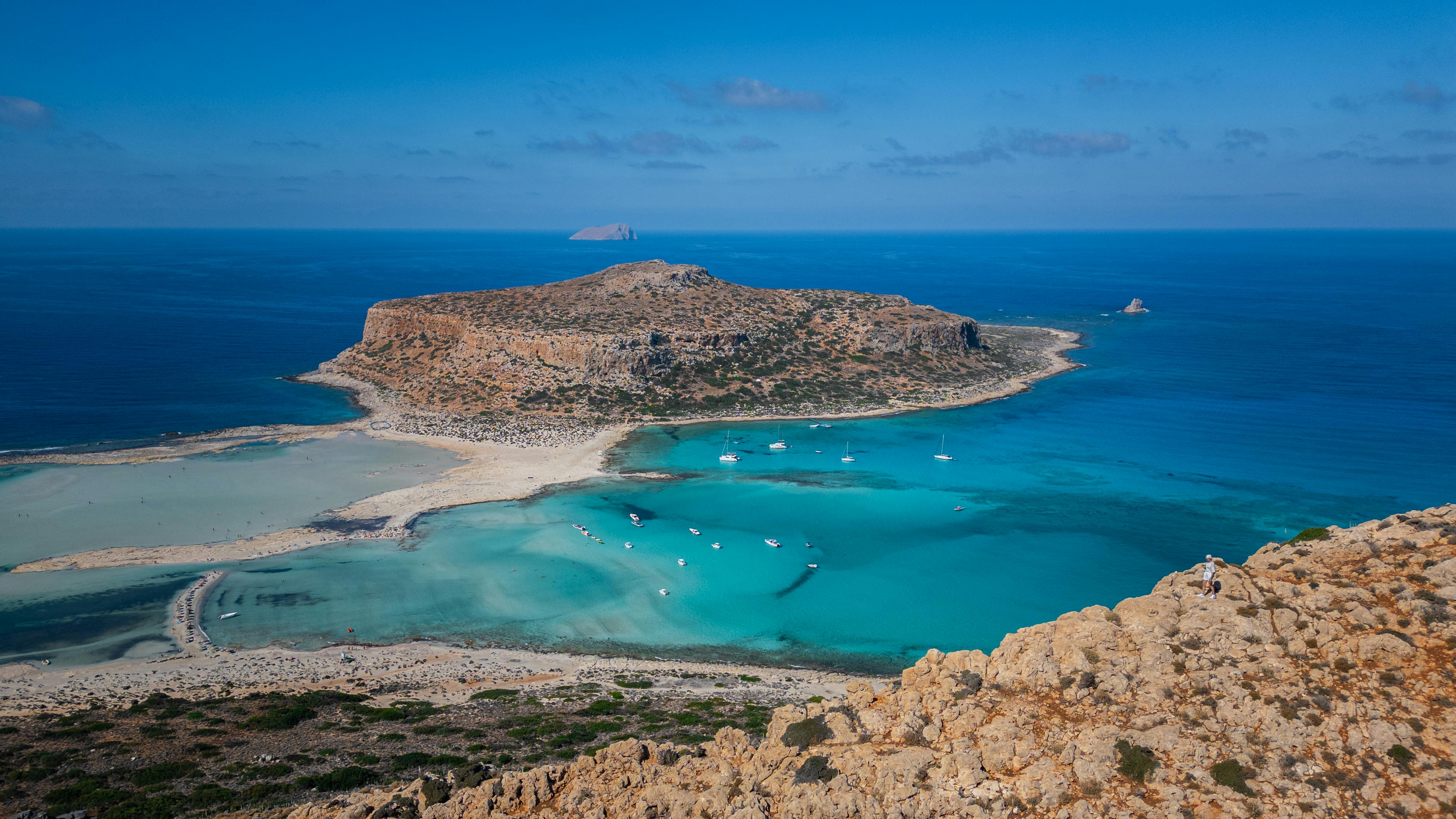 Aerial view of a Greek village coastline with turquoise water, boats, and rocky cliffs in a Mediterranean setting. Aerial view of a Greek village coastline with turquoise water, boats, and rocky cliffs in a Mediterranean setting.