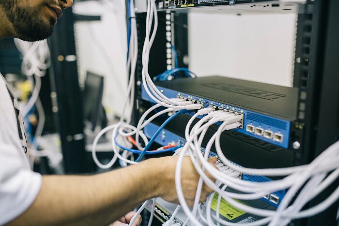 Technician managing network cables at a server rack, illustrating a glitch in the system being exploited.
