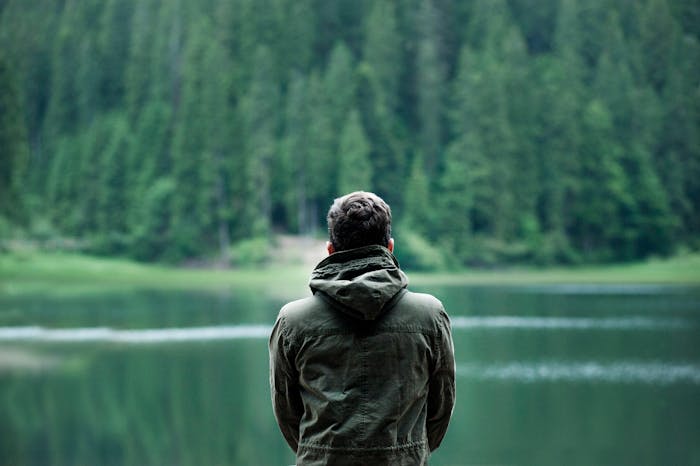 Man in green jacket standing alone by a lake with forest background, symbolizing proof of cheating and ex-girlfriend drama.
