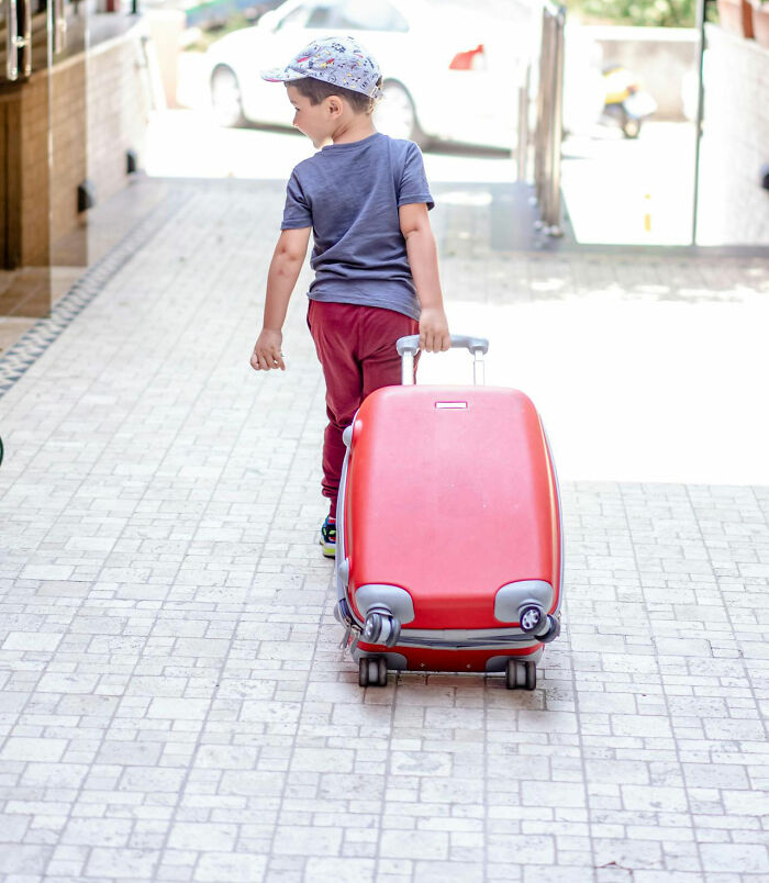 Young boy pulling a red suitcase along a tiled walkway, capturing a moment related to crazy airport stories.