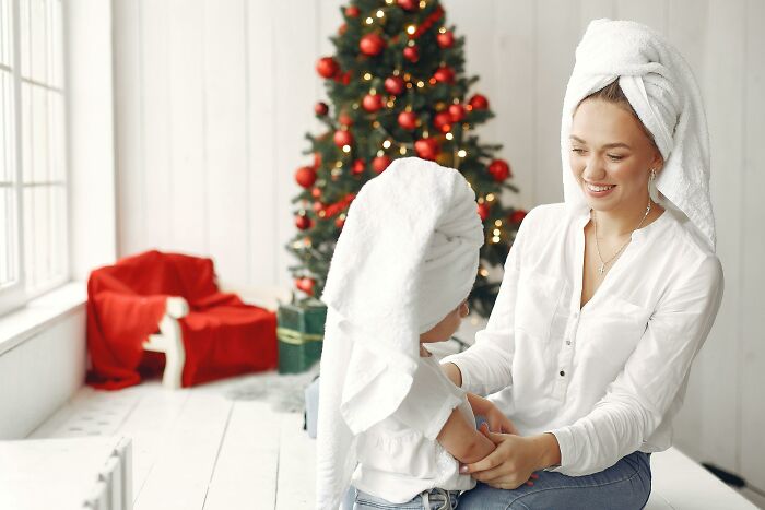 Mother and child with towels on heads by a decorated Christmas tree and wrapped presents during holiday gift time.
