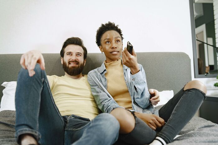 A couple sitting on a couch watching TV together, representing the smartest couch potato quiz concept. A couple sitting on a couch watching TV together, representing the smartest couch potato quiz concept.