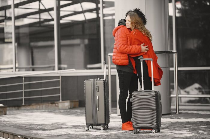 Two travelers in red jackets hugging outside an airport with suitcases, illustrating crazy airport stories.