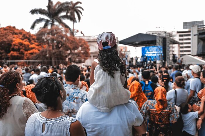 Crowd of people at outdoor event with child on adult’s shoulders, illustrating challenges of modern parenting trends today.