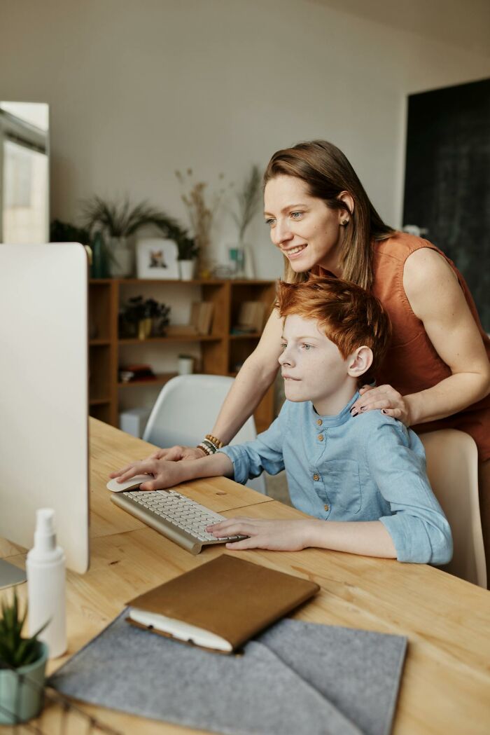 A mother helping her son on a computer at home, illustrating modern parenting trends.