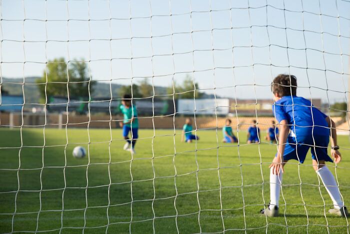 Children playing soccer on a field with a goalie ready, illustrating modern parenting trends in youth sports activities.