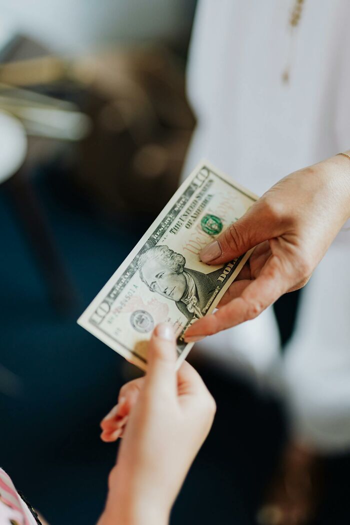 Hand passing a ten-dollar bill to another person illustrating a glitch in the system exploitation scenario.