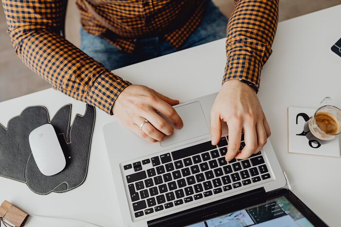 Person wearing a checkered shirt using a laptop, illustrating small design mistakes in user interface and workspace setup.