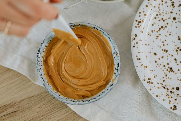 Person stirring smooth peanut butter in a speckled bowl, highlighting the texture in a cozy kitchen setting.
