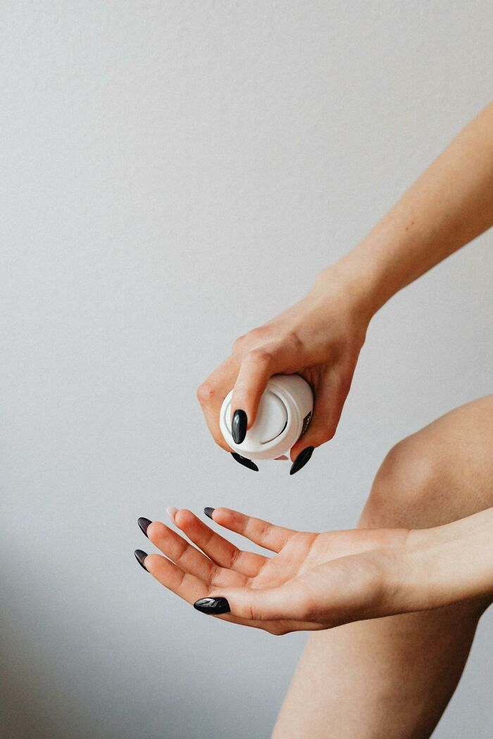 Person with black nails applying cream from a bottle onto their hand, illustrating brilliantly sneaky acts of revenge.