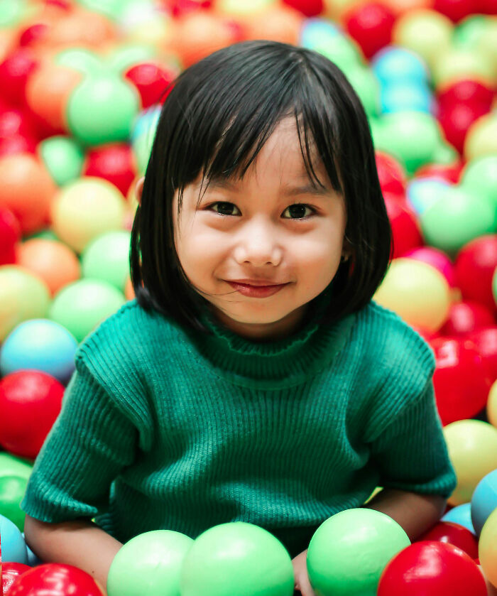 Young child smiling while playing in a colorful ball pit, illustrating the theme of bizarre and unusual names given to children.