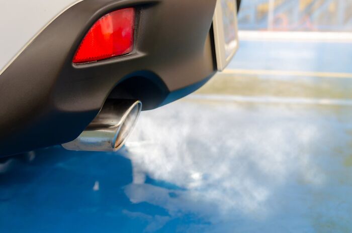 Close-up of a car exhaust pipe emitting smoke, illustrating a brilliantly sneaky act of revenge in a parking area.