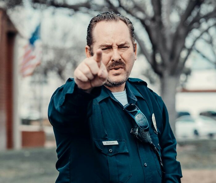 Police officer pointing directly at the camera with a serious expression, representing true stories that sound made up.