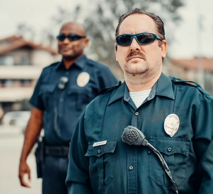 Two security guards wearing sunglasses and uniforms standing outdoors, representing workplace scandals and issues.