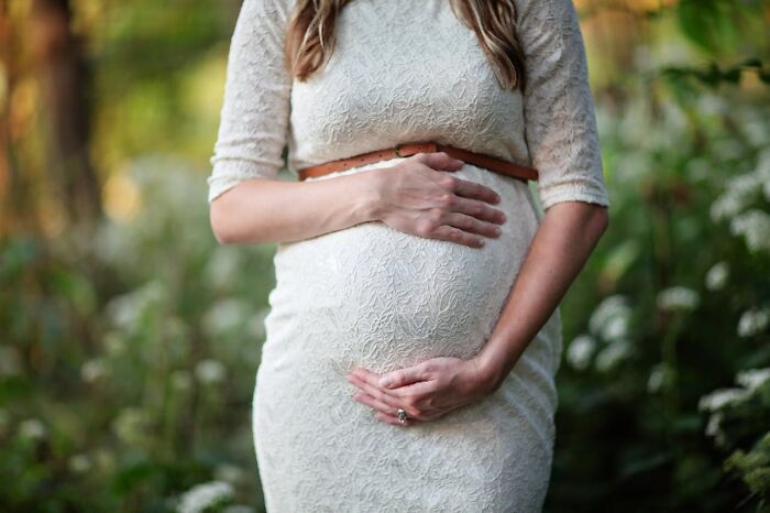 Pregnant woman in a white lace dress holding her belly outdoors, symbolizing disturbing facts people learned unexpectedly.