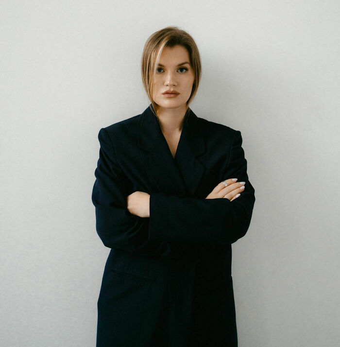 Young woman with a serious expression and arms crossed, displaying pure entitlement against a plain background.