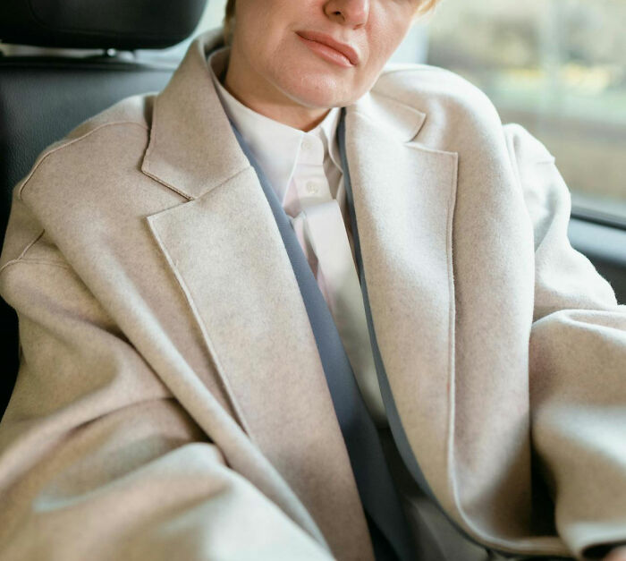Person wearing a beige coat sitting in a car, evoking curiosity about owners of lost things who never returned for them