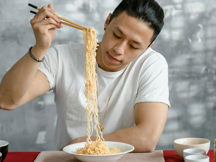 Young man enjoying noodles with chopsticks, highlighting picky eater demands affecting family Christmas menu choices. Young man enjoying noodles with chopsticks, highlighting picky eater demands affecting family Christmas menu choices.