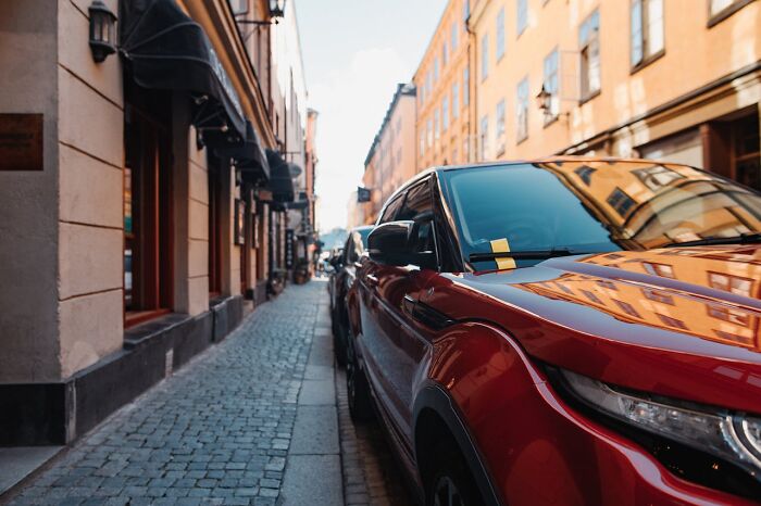 Red car parked on a narrow cobblestone street reflecting buildings, illustrating a glitch in the system concept.
