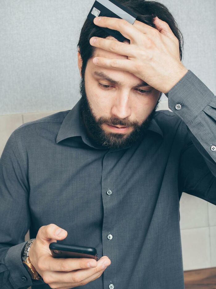 Man holding credit cards to his forehead looking at phone with worried expression, illustrating disturbing facts learned.