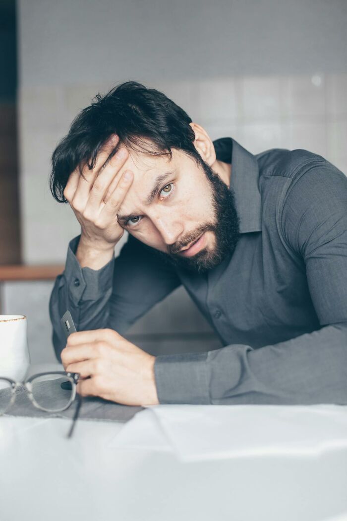 Man looking frustrated and stressed while sitting at a table, displaying pure entitlement in an indoor setting.