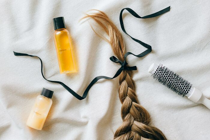 Braided hair tied with a black ribbon surrounded by shampoo bottles and a round hairbrush, illustrating horrible gift ideas.