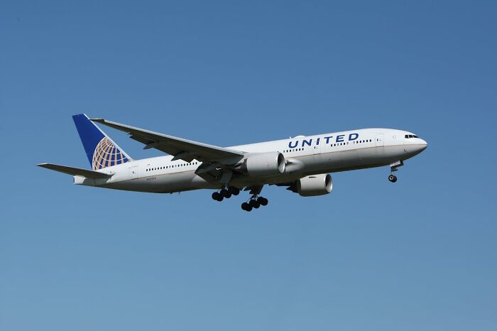 United Airlines airplane in mid-flight with landing gear down against a clear blue sky for crazy airport stories.