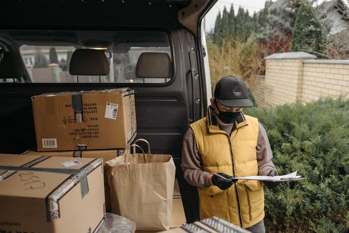 Postal worker wearing a mask and gloves sorting packages and paperwork at the back of a delivery van.