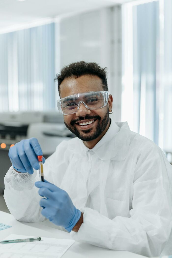 Smiling scientist in protective gear holding a test tube, illustrating funny clever and sassy moments in the heat of the moment