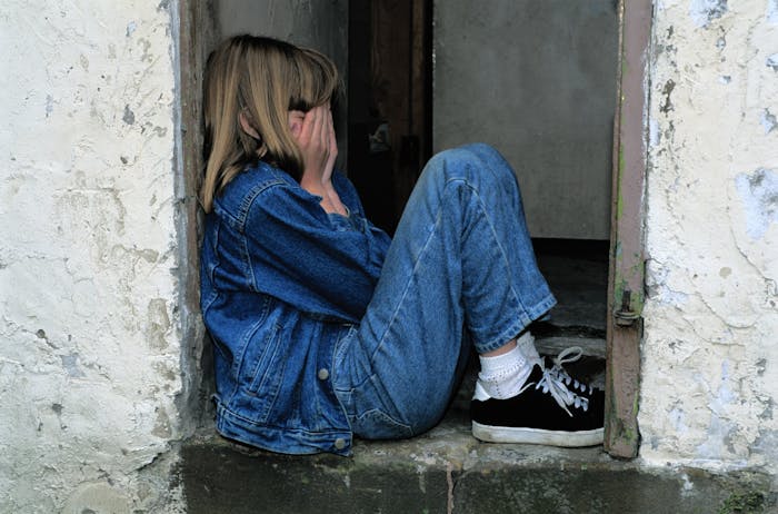 Young girl in denim jacket sitting on doorstep covering her face, reflecting a daughter doing much for her mother. Young girl in denim jacket sitting on doorstep covering her face, reflecting a daughter doing much for her mother.