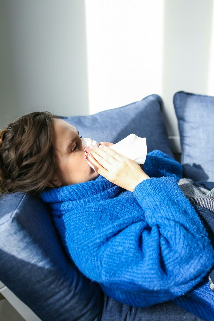 Woman in blue sweater lying on couch blowing nose, illustrating disturbing facts people learned against their will concept.