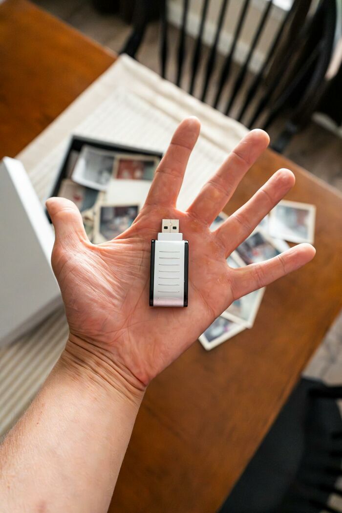 Hand holding a USB drive with blurred photos on a wooden table, capturing funny clever sassy moments in the heat.