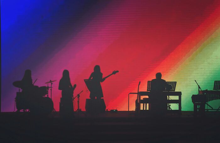 Silhouettes of a live band performing on stage with colorful gradient lights highlighting the music scene and band names. Silhouettes of a live band performing on stage with colorful gradient lights highlighting the music scene and band names.