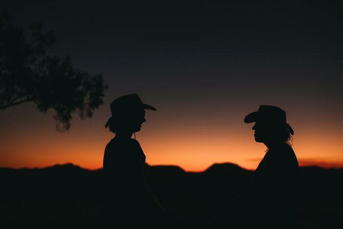 Silhouettes of two people wearing cowboy hats facing each other against a colorful sunset background showcasing famous characters. Silhouettes of two people wearing cowboy hats facing each other against a colorful sunset background showcasing famous characters.