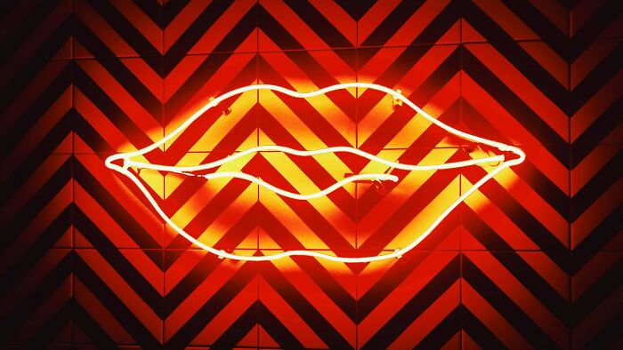 Neon lips sign glowing bright orange against a geometric patterned wall, illustrating facial recognition challenge.