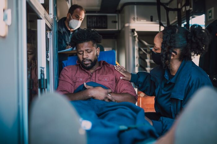 Man clutching stomach in pain inside ambulance, receiving care from emergency responders showing everyday health dangers.