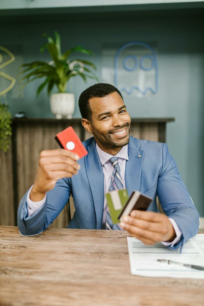 Man smiling and holding multiple credit cards at a desk, showcasing a glitch in the system opportunity with confidence.