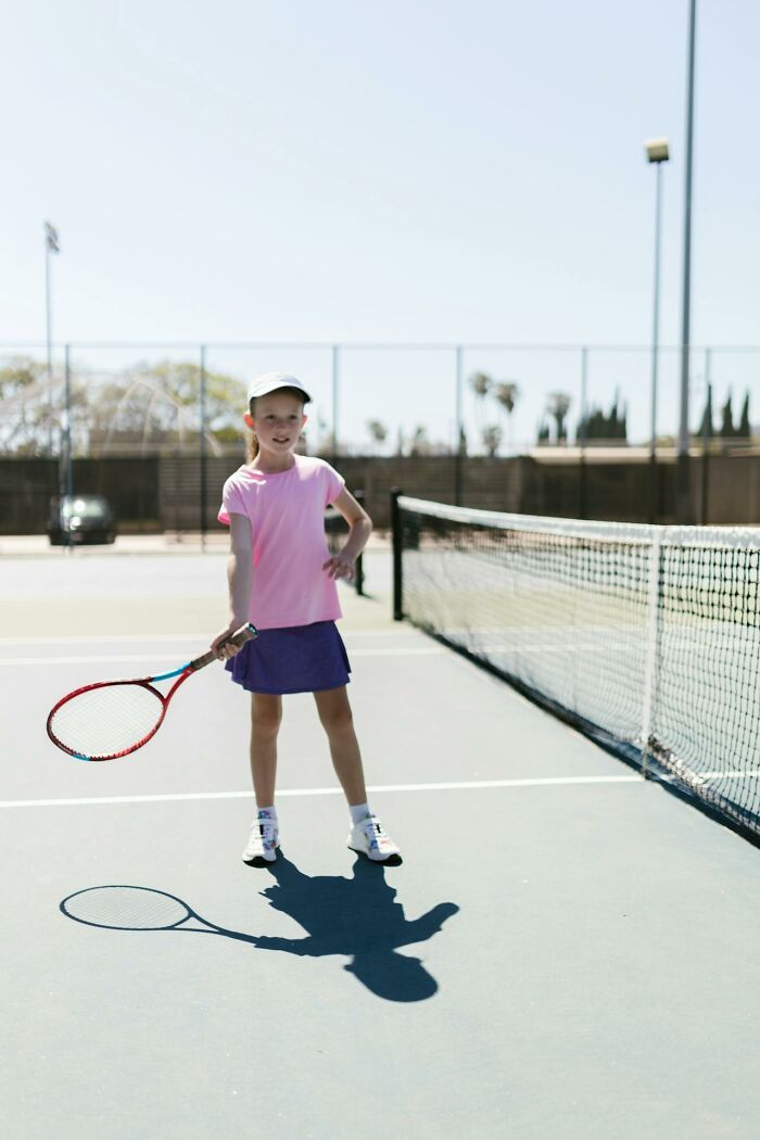Young girl playing tennis on court during outdoor activity, illustrating modern parenting trends in youth sports.