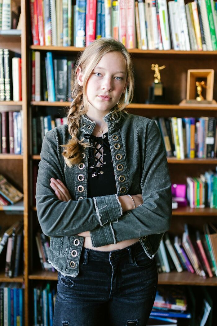 Teen girl with braid and sassy expression standing confidently in front of bookshelves, embodying clever attitude in the moment