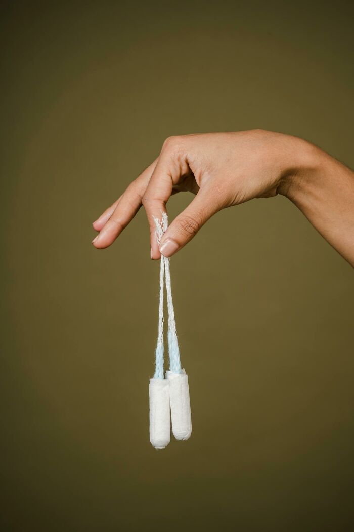 Hand holding two tampons by their strings against a plain background, representing brilliantly sneaky acts of revenge.